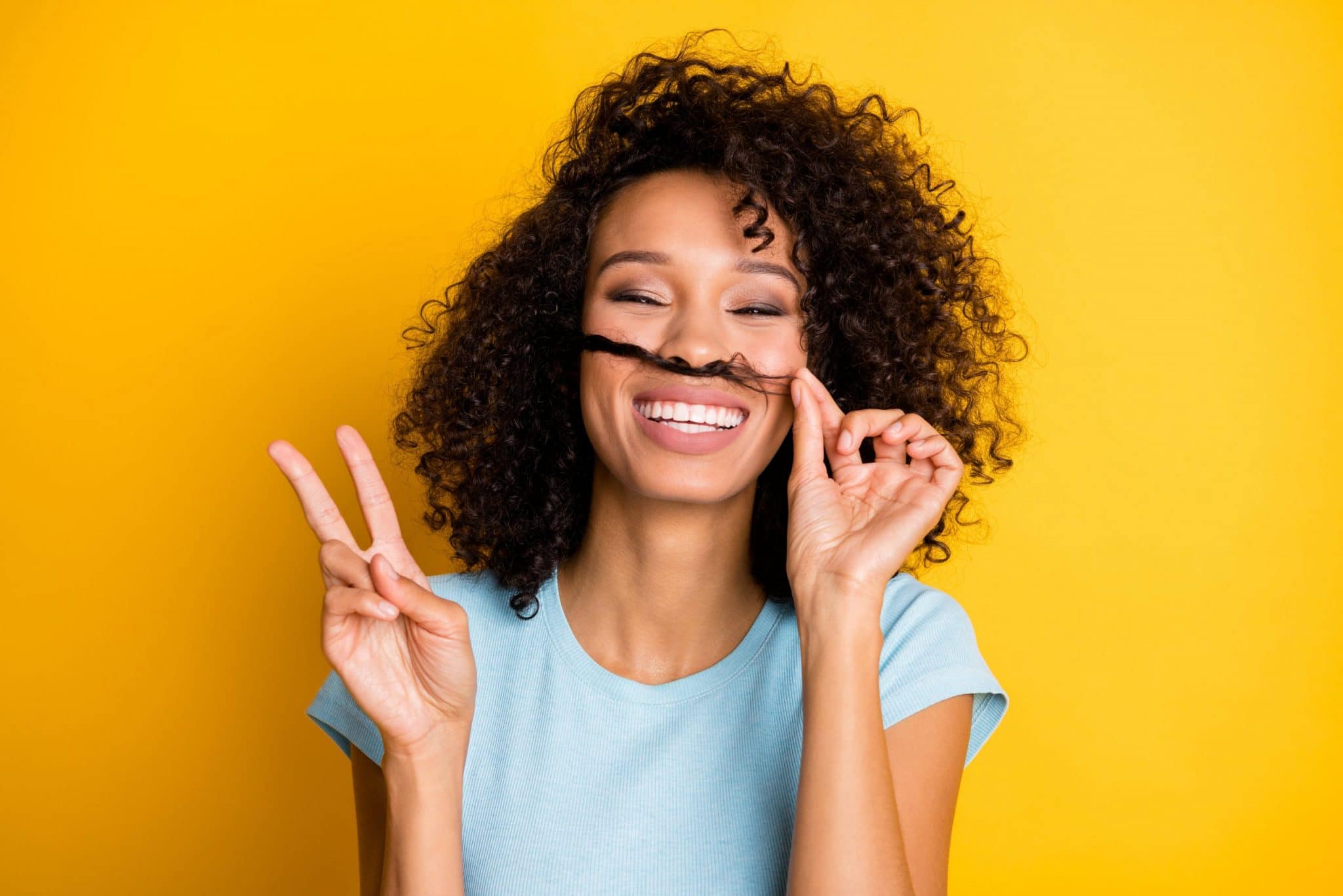 femme qui sourit avec les doigts en signe de victoire et qui fait semblant d'avoir une moustache avec ses cheveux