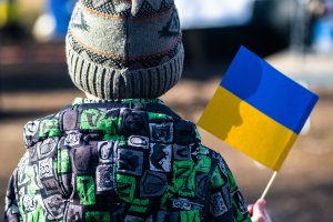 Child or kid with winter clothes, hat and Ukrainian flag, profile of the child is on the flag. War in Ukraine, refugee, refugees concept