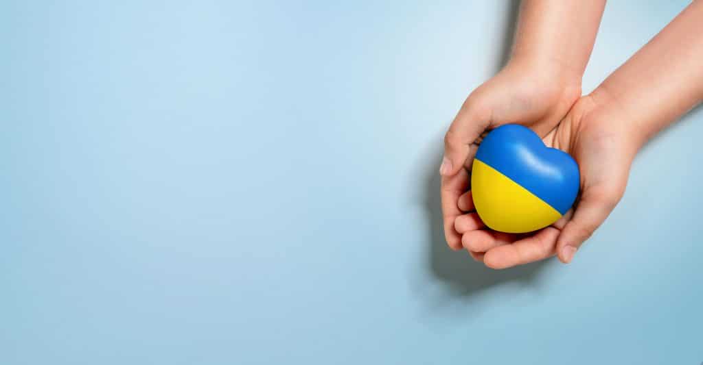 High angle view of human hands holding heart, painted with ukraine flag colors isolated on blue background