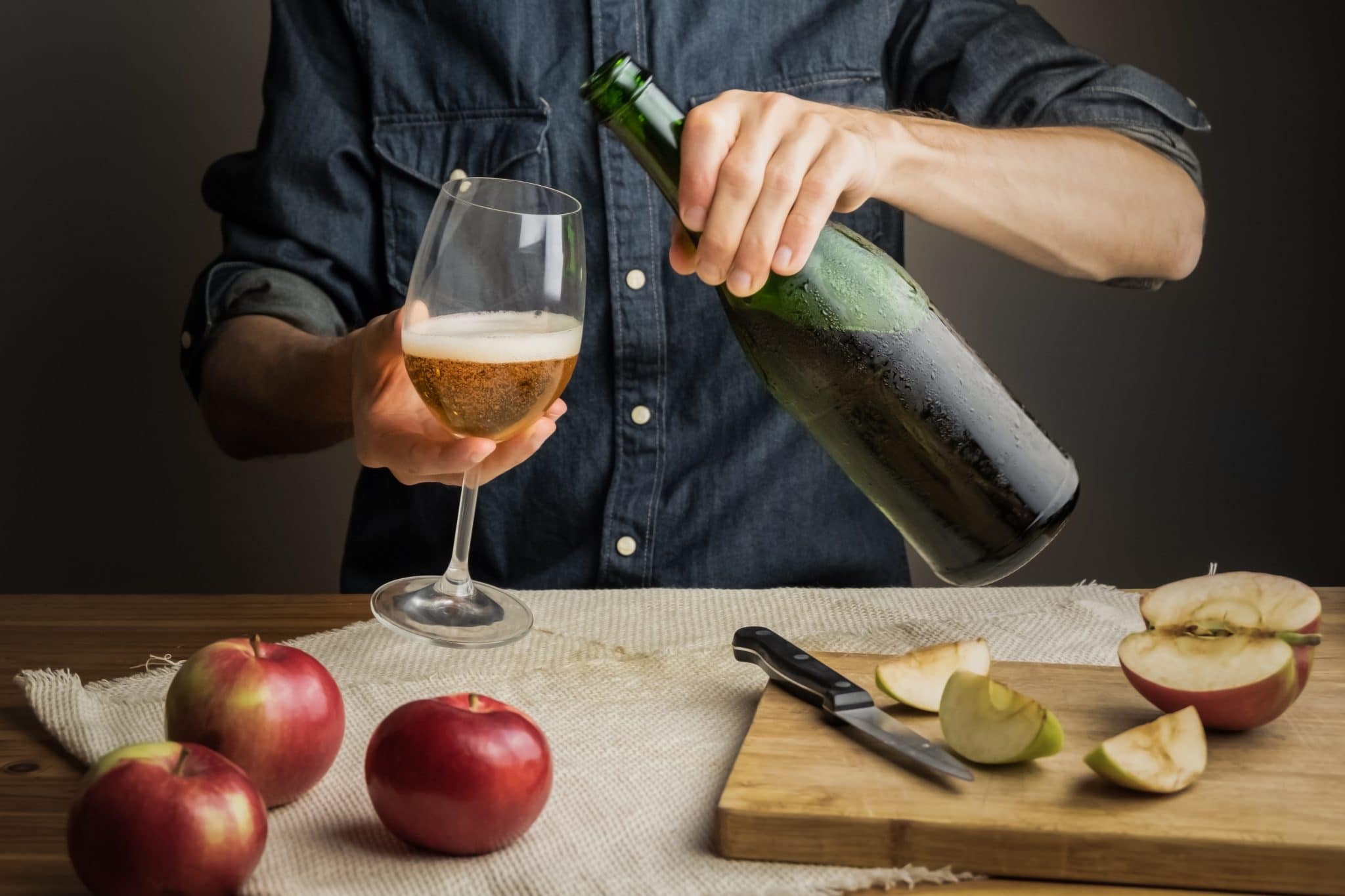 Male hands pouring premium cidre in wine glass above rustic wood table. Tasting vintage apple cider out of ice cold bottle