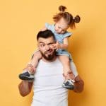 naughty behavior. parent cannot handle with kid with much energy. girl tiuching her dad's eyes while sittting on shoulders . close up photo. isolated yellow background. unacceptable kind of behaviour