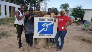 Les jeunes sourds et mal-entendants prennent la pose autour de la pancarte de la Ferme Ecole à Sinthiou Maleme au Sénégal