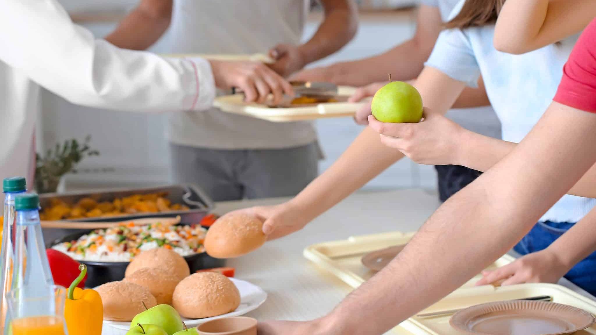 Dans une cantine, plusieurs mains de jeunes personnes se tendent vers des plats à choisir