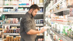 Une homme dans un supermarché lit l'étiquette d'une bouteille de lait