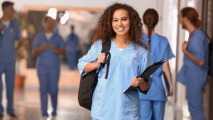 Une étudiante en médecine sourit. Elle porte un sac à dos et un uniforme bleu.