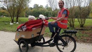 Un bénévole de l'association A vélo sans âge pilote un triporteur dans un parc.
