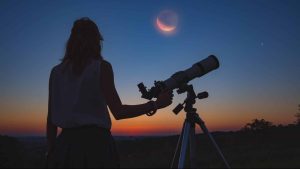 femme de dos tient un telescope et regarde un ciel de nuit avec eclipse lunaire