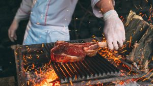 Une homme cuit de la viande rouge au barbecue