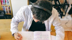 jeune homme porte un casque audio et travaille sur cahier et ordinateur