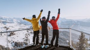 Trois amis en tenue de ski levent les mains en l'air. Ils sont sur une balustrade au milieu de la montagne à la staton de ski des Gets qui interdit de fumer sur les pistes et remontées mécaniques.