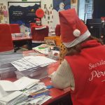 La lutine du Père Noël est en train d'écrire une lettre. Elle est de dos et sur son gilet il y a écrit Secrétariat du Père Noël