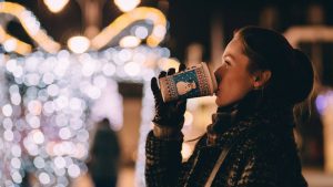 Scène d'hiver : une femme boit dans un verre bonhomme de neige. Illuminations en fond.