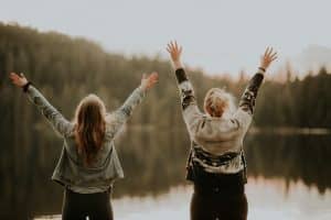 Deux femmes les bras en l'air font face à un lac et expriment leur bonheur