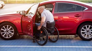 Une personnes handicapée accède à sa voiture sur une place de parking PMR.