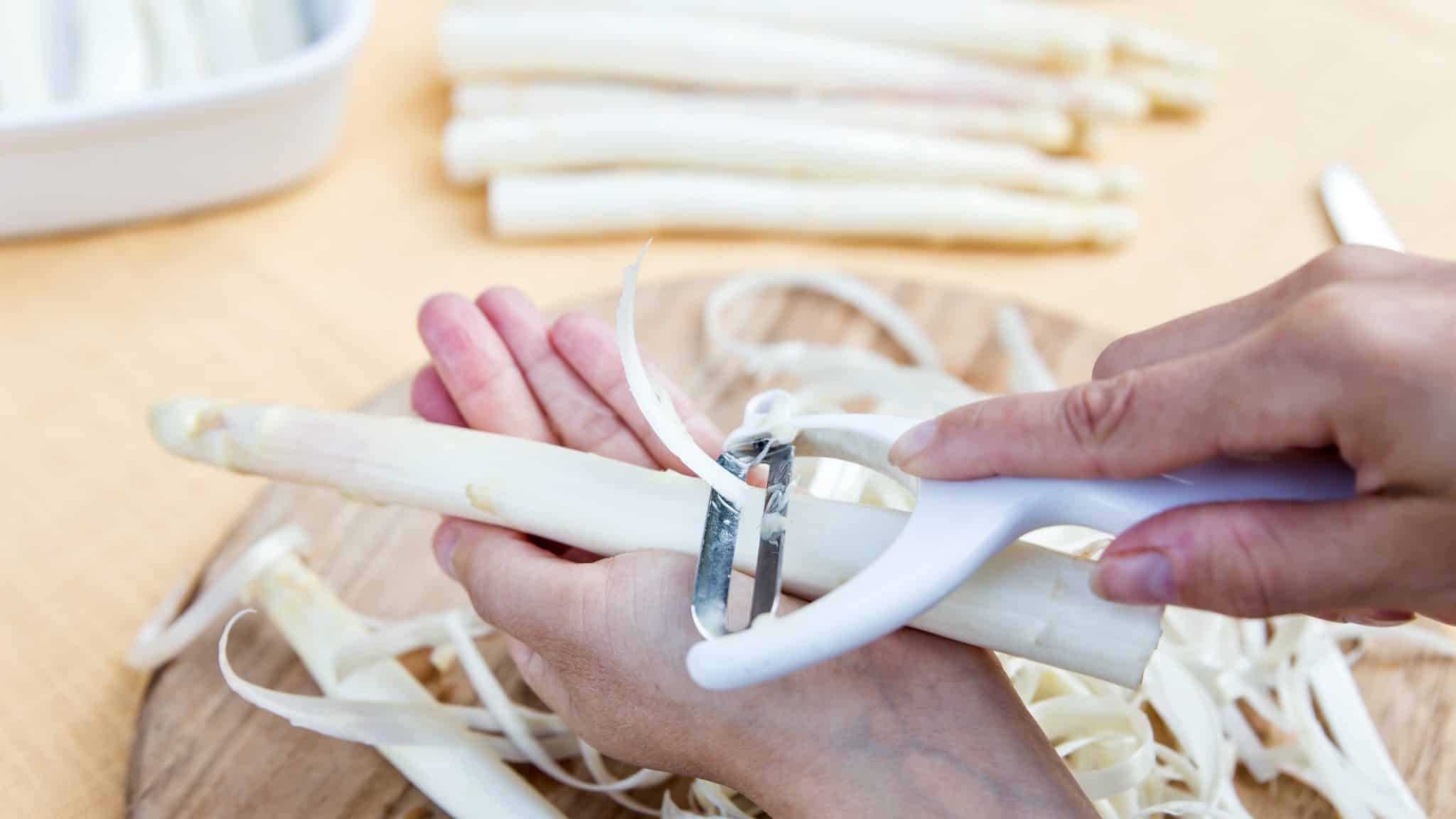 Une main tient une asperge blanche, une seconde l'épluche