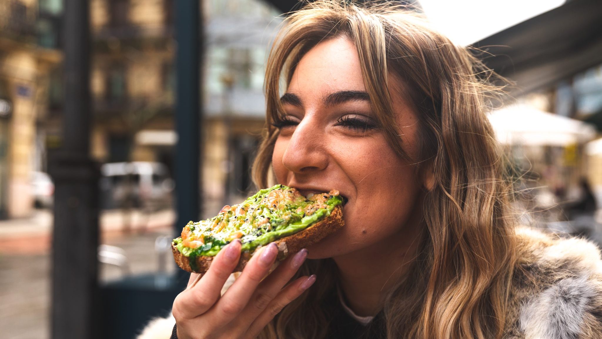 Une femme mange une tartine avec de l'avocat.