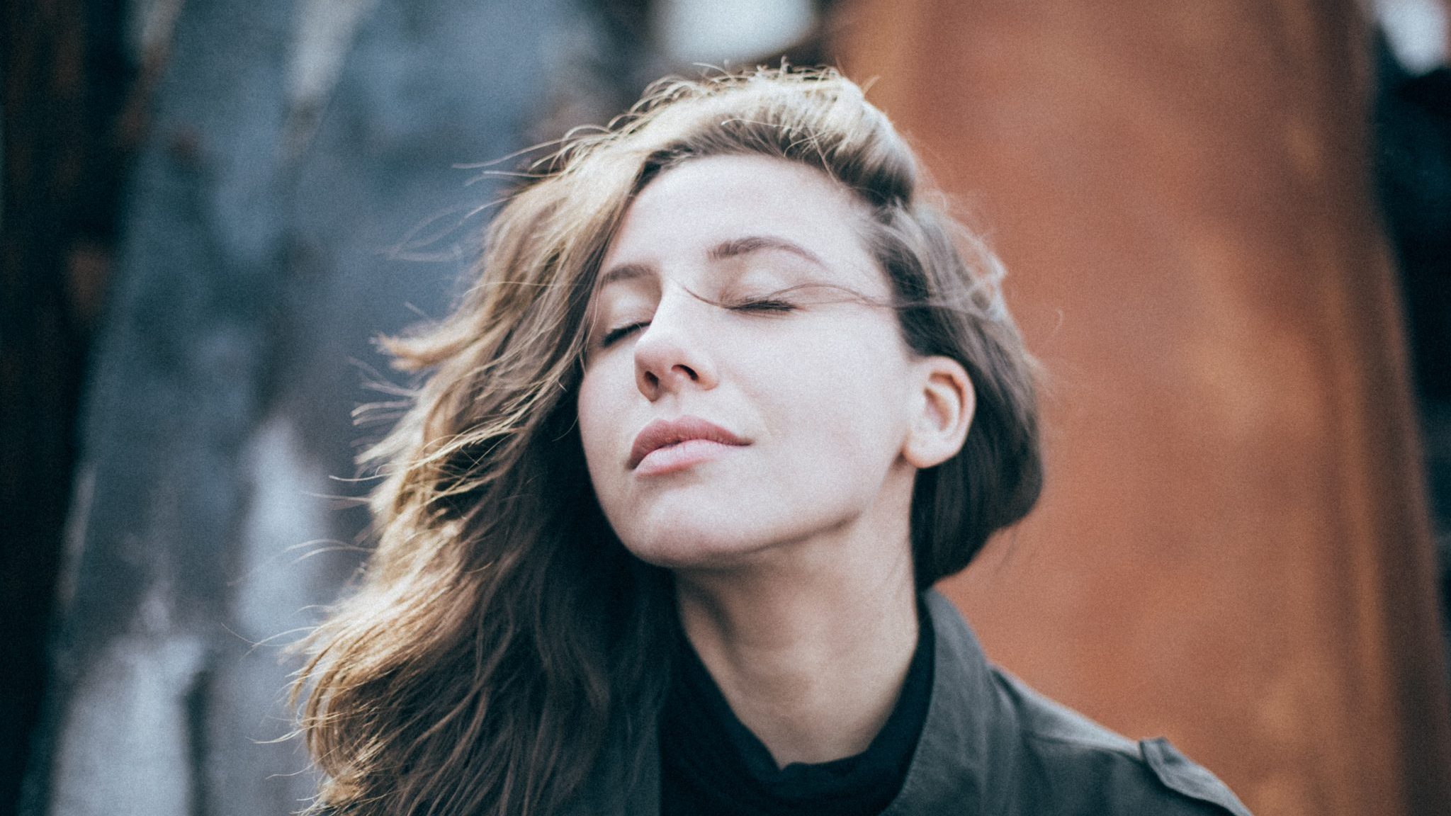 Une femme ferme les yeux, elle a le vent dans ses cheveux