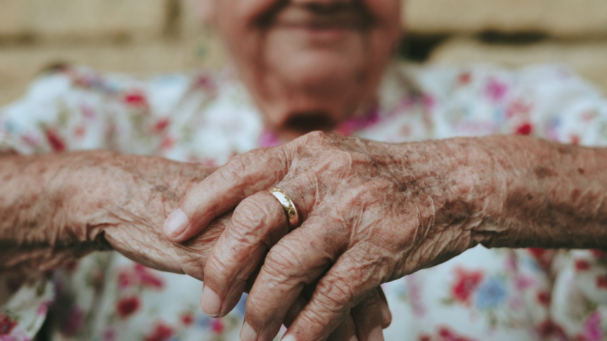 au premier plan il y a les mains jointes d'une personne âgée