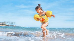 Une petite fille brune cours dans l'eau en maillot de bain avec des bouées autour d'elle