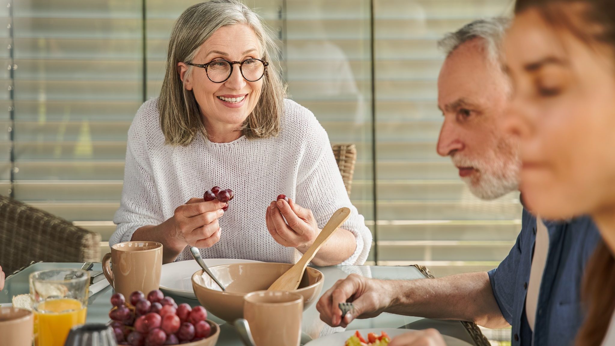 Une femme attablée mange du raisin.