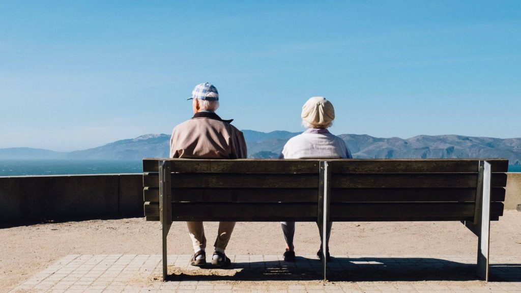 deux personnes âgées assisent sur un banc face à une montagne