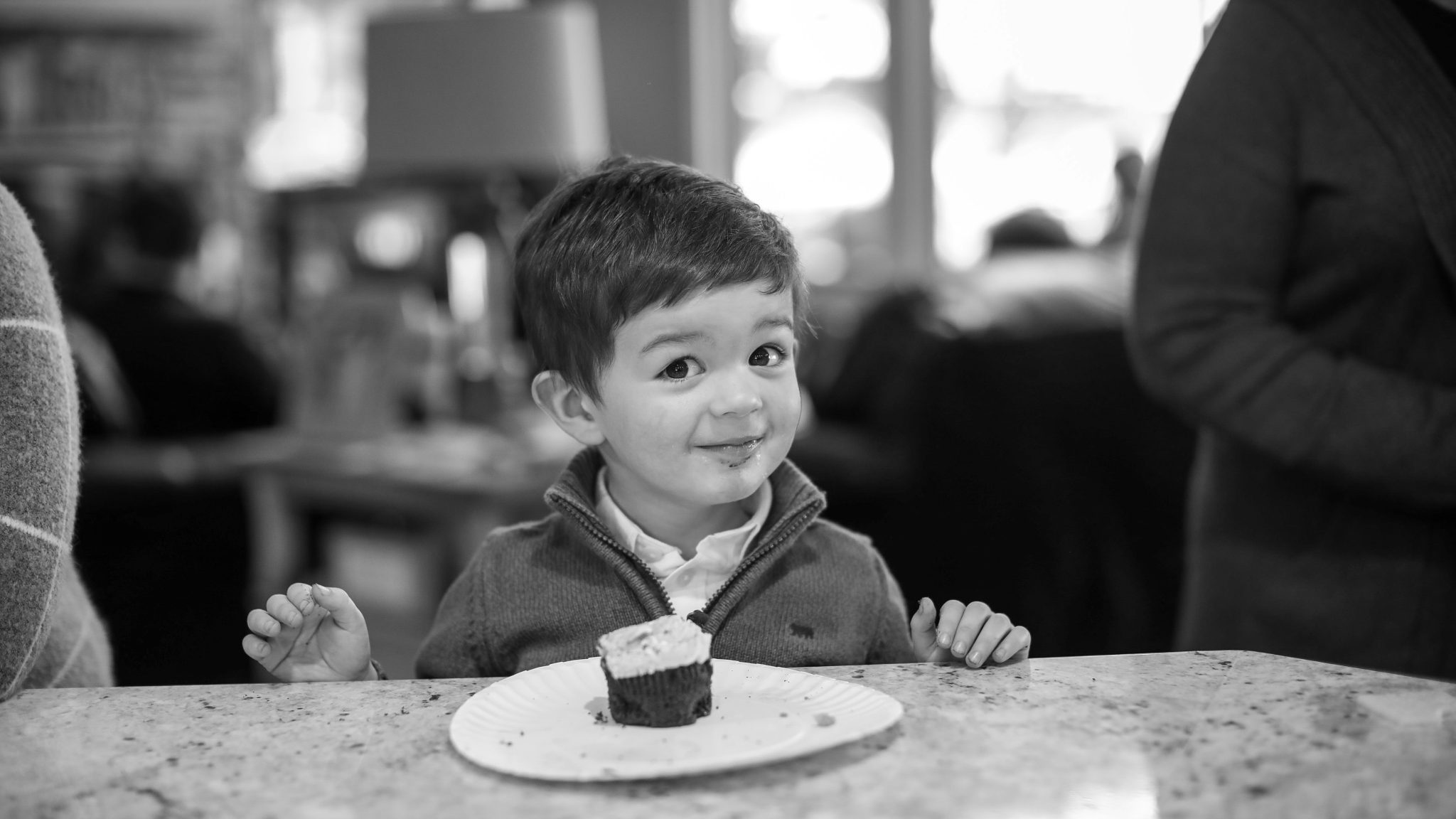 a little boy sitting at a table with a cupcake in front of him