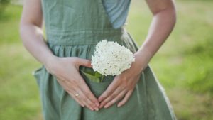 gardening and profession concept - young woman in apron holding flowers in the garden in summer