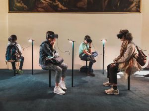 Quatre personnes assisent portent un casque de réalité virtuelle dans ce qui semble être un musée.