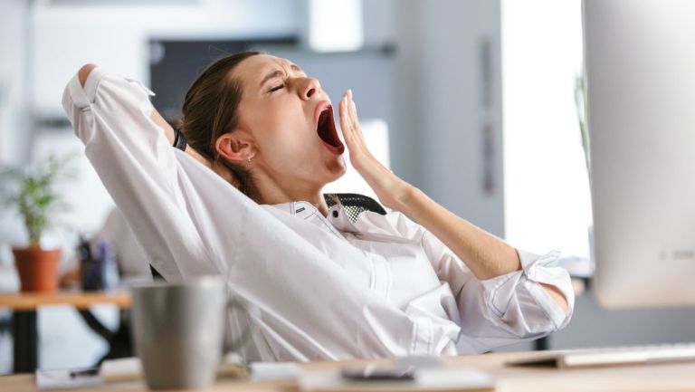 Une femme au travail qui baille sur son bureau.