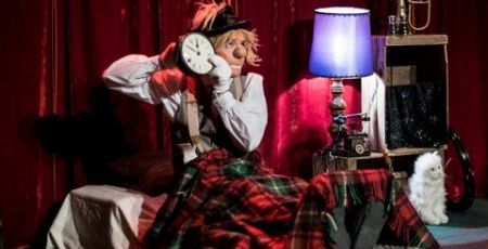 Clown sur scène allongé dans son lit avec un réveil à la main