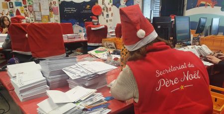 La lutine du Père Noël est en train d'écrire une lettre. Elle est de dos et sur son gilet il y a écrit Secrétariat du Père Noël
