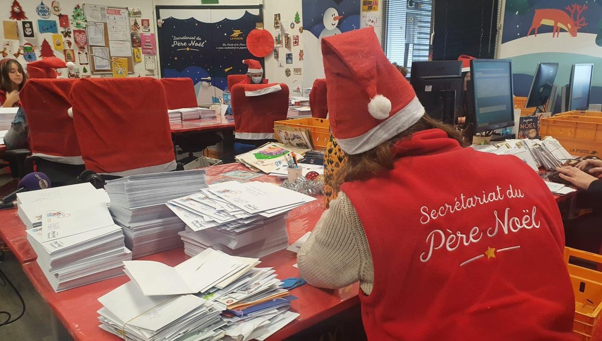 La lutine du Père Noël est en train d'écrire une lettre. Elle est de dos et sur son gilet il y a écrit Secrétariat du Père Noël
