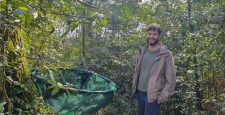 Thomas Caignard, post-doctorant à l’UMR Biogéco à l’université de Bordeaux et de l’INRAe pose à côté d'un arbre de la forêt urbaine de Floirac. Sur cet arbre il y a un filet accroché pour récupérer les glands