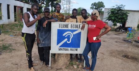 Les jeunes sourds et mal-entendants prennent la pose autour de la pancarte de la Ferme Ecole à Sinthiou Maleme au Sénégal