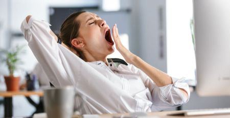 Une femme au travail qui baille sur son bureau.