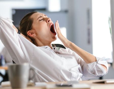 Une femme au travail qui baille sur son bureau.