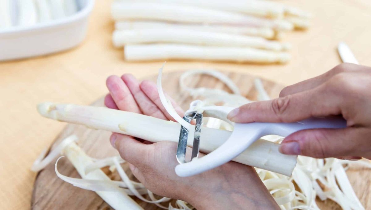 Une main tient une asperge blanche, une seconde l'épluche