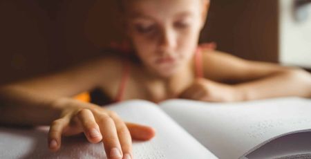 Une enfant malvoyante lit un ouvrage en braille.