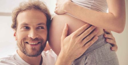 Père qui pose son oreille contre le ventre de sa femme enceinte.