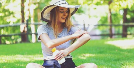 Une femme dans un parc met de la crème solaire.