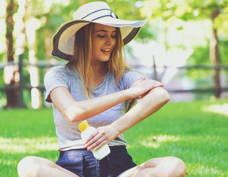 Une femme dans un parc met de la crème solaire.