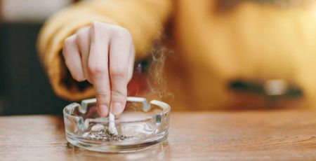 Une femme écrase une cigarette dans un cendrier.