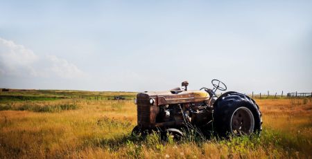 Un vieu tracteur rouillé est posé au milieu d'une prairie aux herbes hautes et jaunies