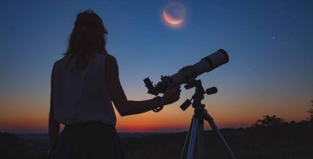 femme de dos tient un telescope et regarde un ciel de nuit avec eclipse lunaire