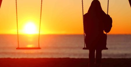 femme de dos, seul sur balaçoire, et autre balançoire vide regarde le couché du soleil
