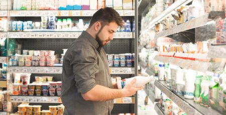 Une homme dans un supermarché lit l'étiquette d'une bouteille de lait