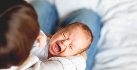 Un bébé pleure dans les bras d'un adulte