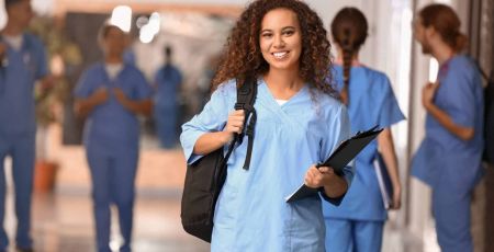 Une étudiante en médecine sourit. Elle porte un sac à dos et un uniforme bleu.