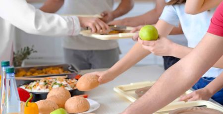 Dans une cantine, plusieurs mains de jeunes personnes se tendent vers des plats à choisir