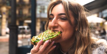 Une femme mange une tartine avec de l'avocat.